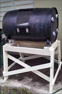 Homemade composting machine built from treated 2x4s and a 55 gallon drum resting on heavy-duty casters.